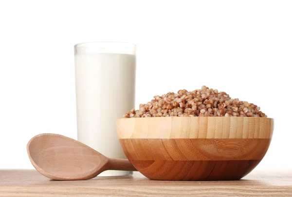 Trigo sarraceno hervido en un tazón de madera con un vaso de leche sobre una mesa de madera isol —  Fotos de Stock