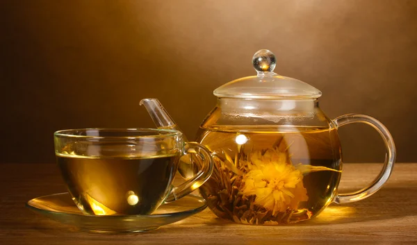 Skleněná konvice a šálek s exotickými zelený čaj na dřevěný stůl na hnědé backgro — Stock fotografie