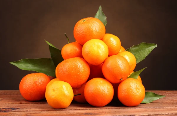 Tangerines avec feuilles sur table en bois sur fond marron — Photo