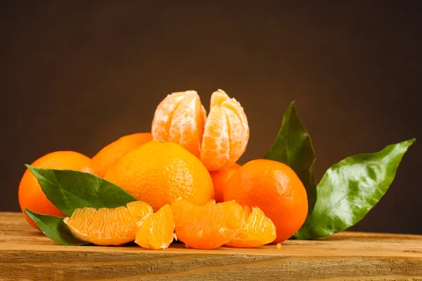 Mandarino con foglie su tavolo di legno su sfondo marrone — Foto Stock