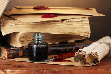 Old books, scrolls, ink pen and inkwell on wooden table on brown background clipart