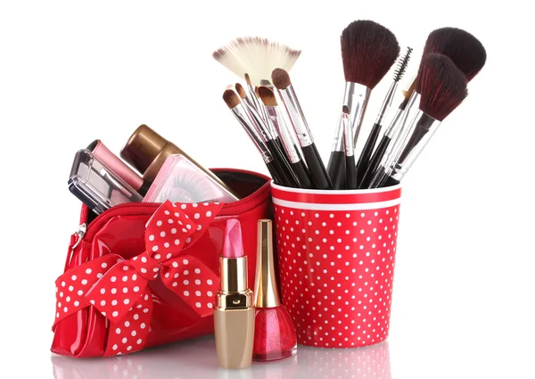 Vidrio rojo con cepillos y bolsa de maquillaje con cosméticos aislados en blanco — Foto de Stock