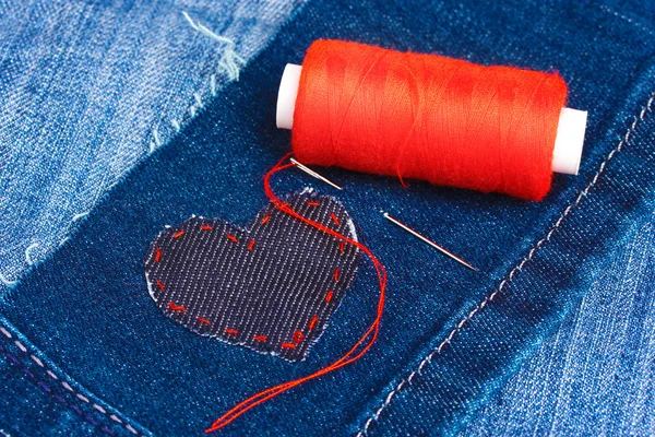 Heart-shaped patch on jeans wiht needle and thread closeup — Stock Photo, Image