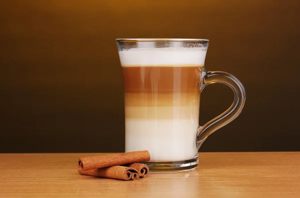 Café con leche fragante en taza de vidrio y canela en mesa de madera en la frente — Foto de Stock