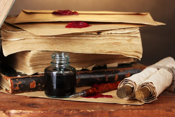 Старые книги, свитки, чернильная ручка и чернильница на деревянном столе на коричневом фоне — стоковое фото