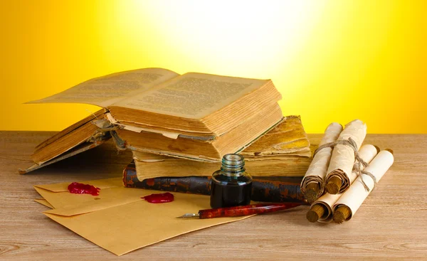 Vecchi libri, pergamene, penna a inchiostro e calamaio su tavolo di legno su sfondo giallo — Foto Stock