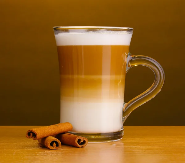 Latte perfumado com latte em copo de vidro e canela na mesa de madeira no fundo marrom — Fotografia de Stock