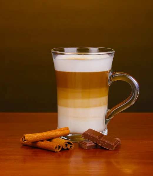 Café con leche perfumada en taza de vidrio con canela y chocolate sobre mesa de madera sobre fondo marrón — Foto de Stock