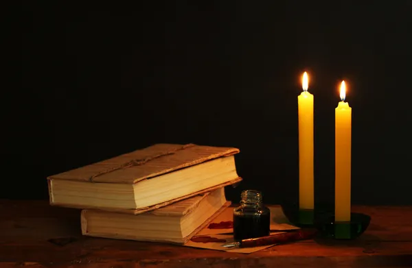 Vecchi libri, pergamene, calamaio penna inchiostro e candele su tavolo di legno su sfondo nero — Foto Stock