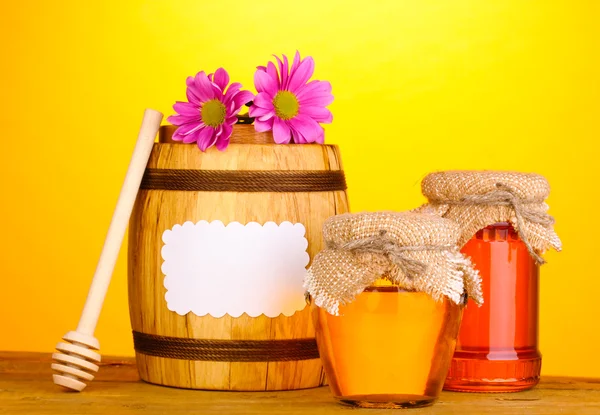 Sweet honey in jars and barrel with drizzler on wooden table on yellow background — Stock Photo, Image