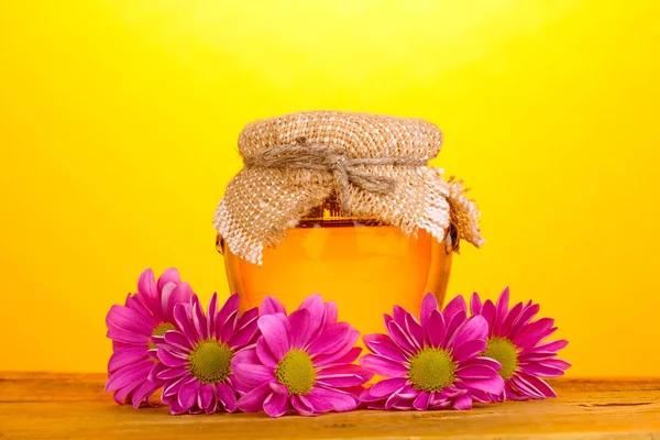 Söt honung i burken på träbord på gul bakgrund — Stockfoto