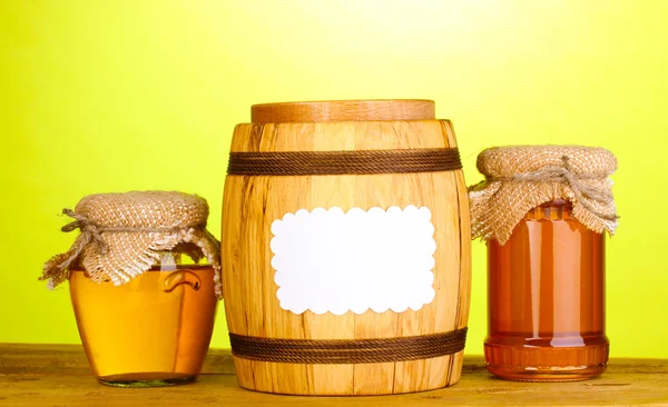 Miel dulce en frascos y barril sobre mesa de madera sobre fondo verde — Foto de Stock