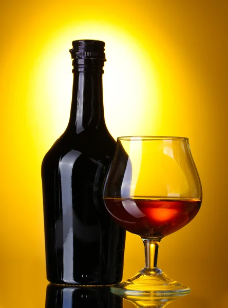 Glas brandy en fles op gele achtergrond — Stockfoto