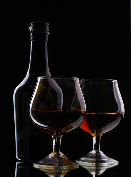 Glasses of brandy and bottle on black background — Zdjęcie stockowe
