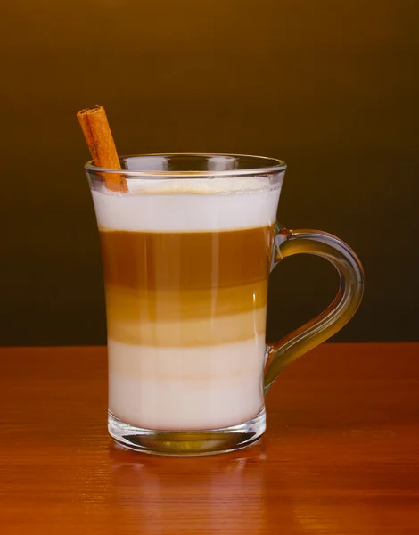 Fragrant сappuccino latte in glass cup and cinnamon on wooden table on brown background — Stock Photo, Image