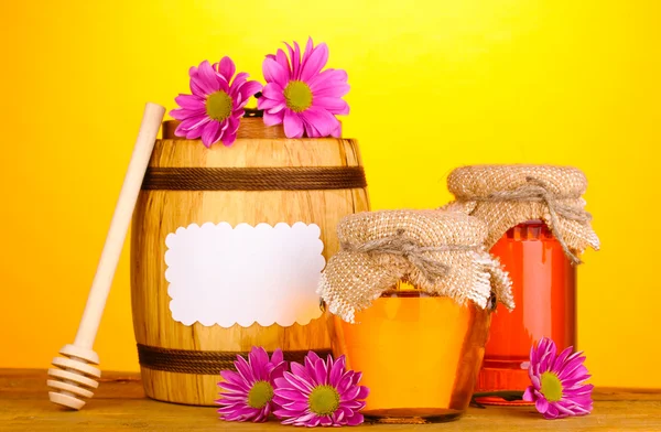 Zoete honing in potten en vat met drizzler op houten tafel op gele achtergrond — Stockfoto