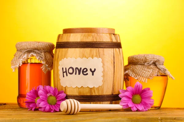 Miel dulce en barril y frascos con rociador sobre mesa de madera sobre fondo amarillo —  Fotos de Stock