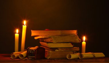 Pile of old books with candle and scroll in dark clipart