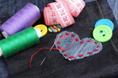 Heart-shaped patch on jeans with threads and buttons closeup clipart