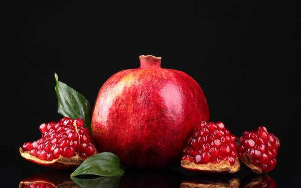 Ripe pomegranate fruit with leaves on black background — Stock Photo, Image