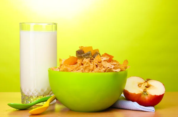 Leckere Cornflakes in grüner Schüssel, Apfel und Milchglas auf Holztisch auf grünem Hintergrund — Stockfoto