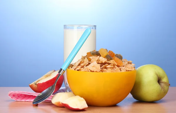在黄色碗、 苹果和一杯牛奶在蓝色背景上的木桌上的美味玉米片 — 图库照片