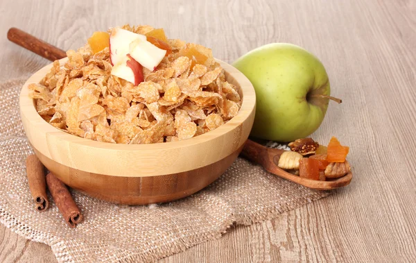 Gustosi cornflakes in ciotola con frutta secca, bicchiere di latte e mela sul tavolo di legno — Foto Stock