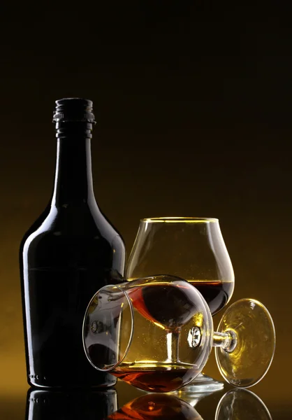 Glasses of brandy and bottle on yellow background — Stock Photo, Image