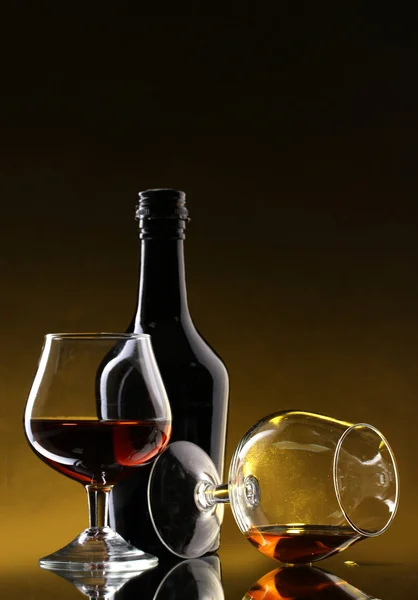 Okulary z brandy i butelka na żółtym tle — Zdjęcie stockowe