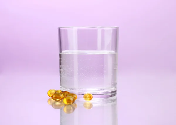 Glas Wasser und Pillen auf violettem Hintergrund — Stockfoto