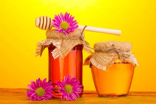 Sweet honey in jars with drizzler on wooden table on yellow background — Stock Photo, Image