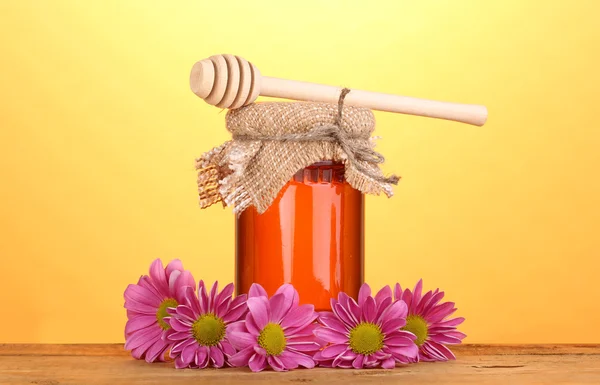 Süßer Honig im Glas mit Nieselregen auf Holztisch auf gelbem Hintergrund — Stockfoto