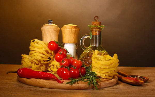 Nouilles dans un bol, pot d'huile, épices et légumes sur table en bois sur fond brun — Photo