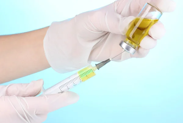 Syringe and medical ampoule in hands on blue background — Stock Photo, Image