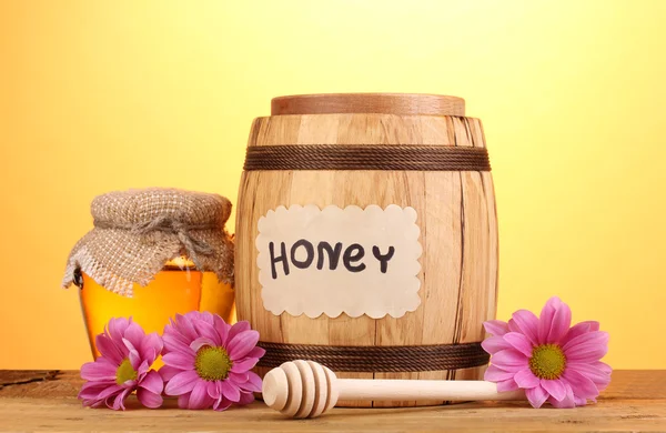 Dolce miele in botte e vaso con drizzler su tavolo in legno su fondo giallo — Foto Stock