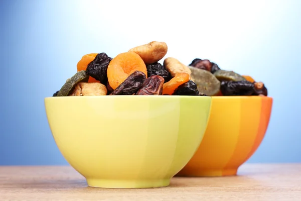 Сушеные фрукты в ярких чашах на деревянном столе на голубом фоне — стоковое фото