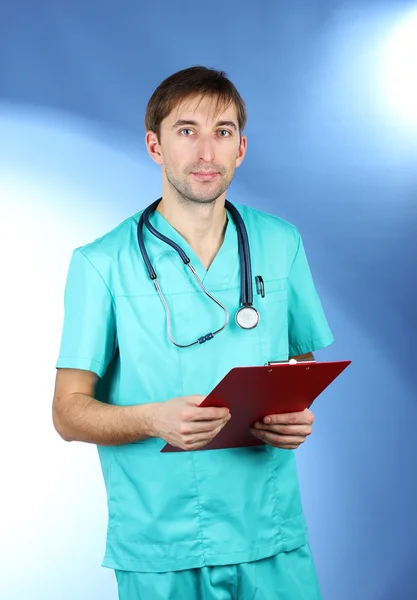 Fiatal orvos ember sztetoszkóp és mappa kék háttérrel — Stock Fotó