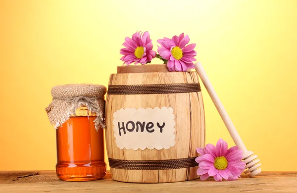 Miel dulce en barril y tarro con rociador sobre mesa de madera sobre fondo amarillo — Foto de Stock