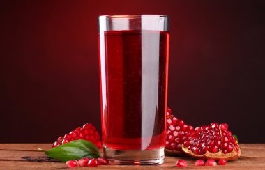 Ripe pomergranate and glass of juice on wooden table on red background clipart