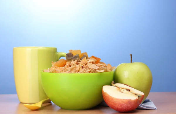 Смачні кукурудзяні пластівці в зеленій мисці, яблука та склянка молока на дерев'яному столі на синьому фоні — стокове фото