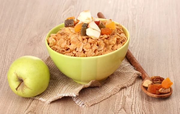 Flocos de milho saborosos em tigela com frutas secas e maçã na mesa de madeira — Fotografia de Stock