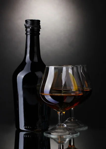 Vasos de brandy y botella sobre fondo gris — Foto de Stock