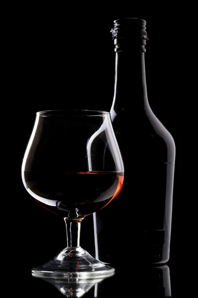 Стакан бренди и бутылка на черном фоне — стоковое фото