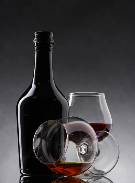 Vasos de brandy y botella sobre fondo gris — Foto de Stock