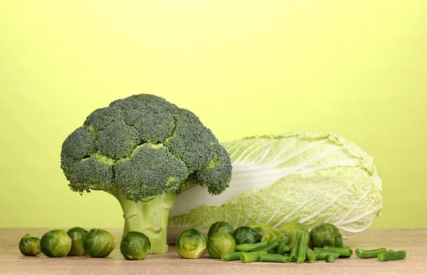 Frischer Brokkoli und Kohl auf Holztisch auf grünem Hintergrund — Stockfoto