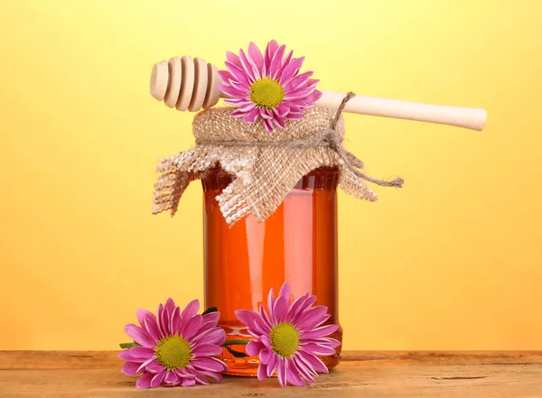 Sladký medu ve sklenici s drizzler na dřevěný stůl na žlutém podkladu — Stock fotografie