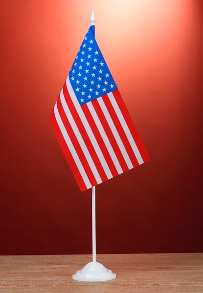 लाल पृष्ठभूमि पर लकड़ी की मेज पर खड़े अमेरिकी ध्वज — स्टॉक फ़ोटो, इमेज