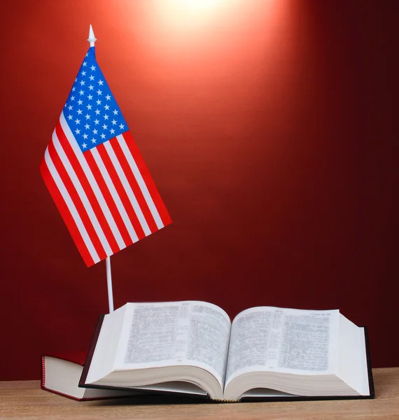 Americká vlajka na stojanu a knihy na dřevěný stůl na červeném pozadí — Stock fotografie