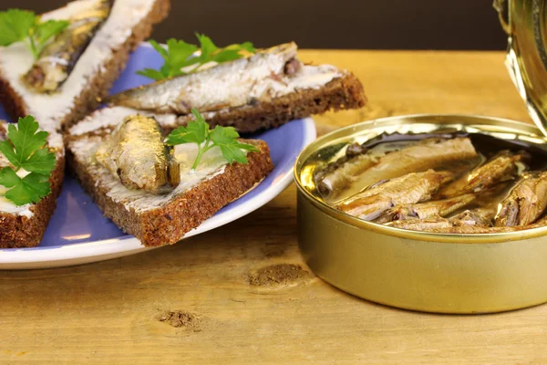 stock image Tasty sandwiches with sprats on plate on wooden table on brown background