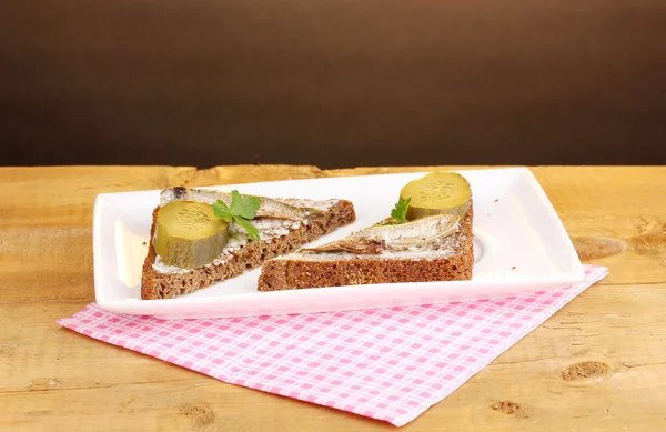 Sabrosos sándwiches con espadines en plato sobre mesa de madera sobre fondo marrón —  Fotos de Stock